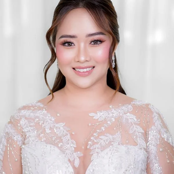 Woman in an embroidered white gown with pink blush, defined lashes and a swept-back hairstyle