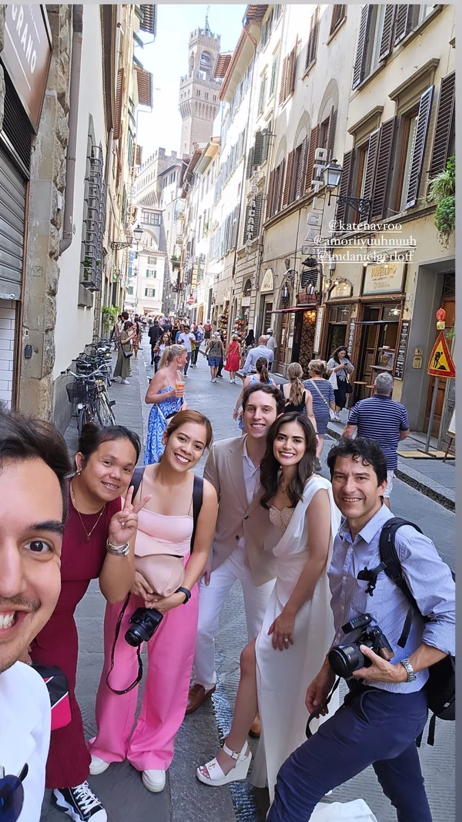 Group photograph with a couple and camera-carrying companions on a narrow street lined with shuttered buildings