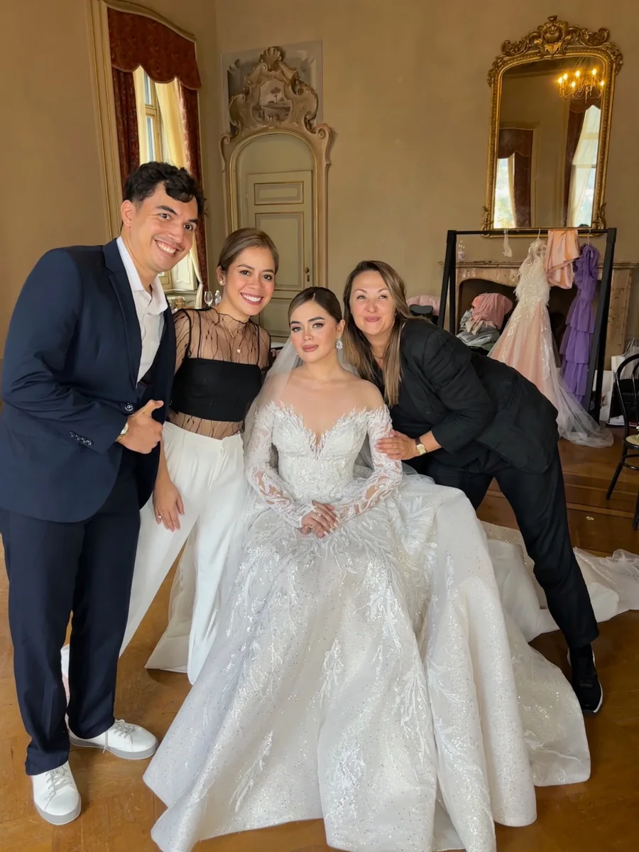 Bride in a beaded white gown posing with three companions in an ornate preparation room