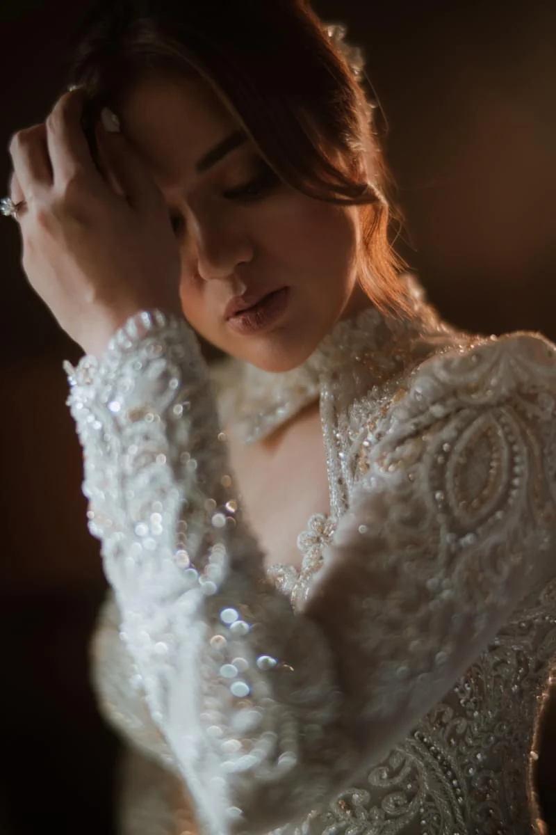 Portrait with eyes lowered and a hand in the hair, wearing a detailed beaded white gown and jeweled collar