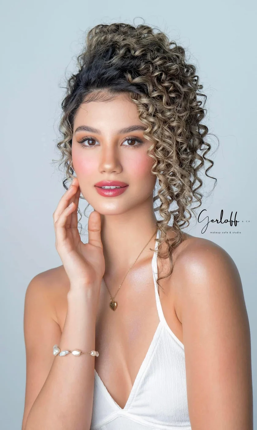 Beauty portrait with a high curly updo, defined lashes, rosy cheeks and a white halter top