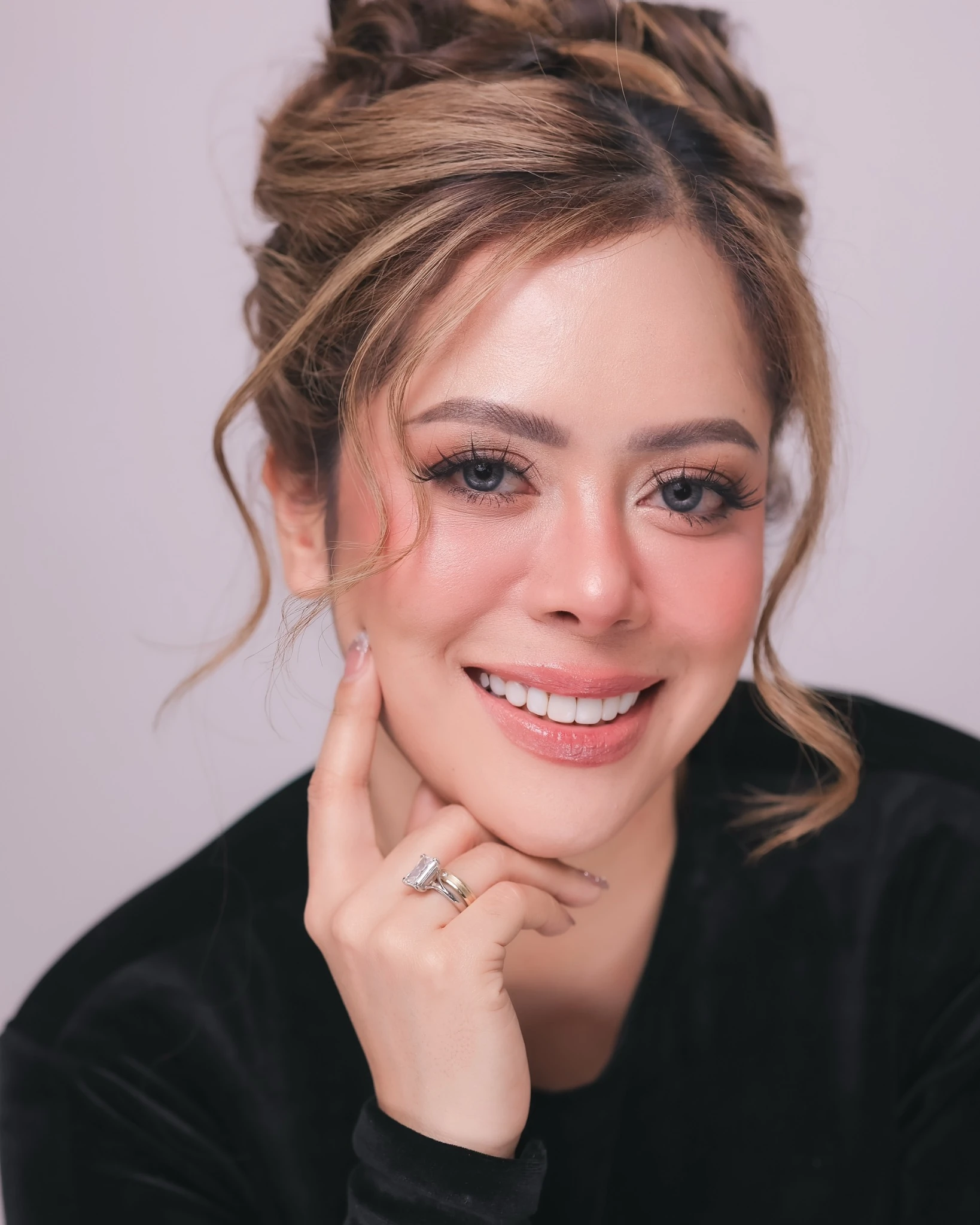 Smiling beauty portrait with rosy makeup, a soft updo and a hand resting at the chin