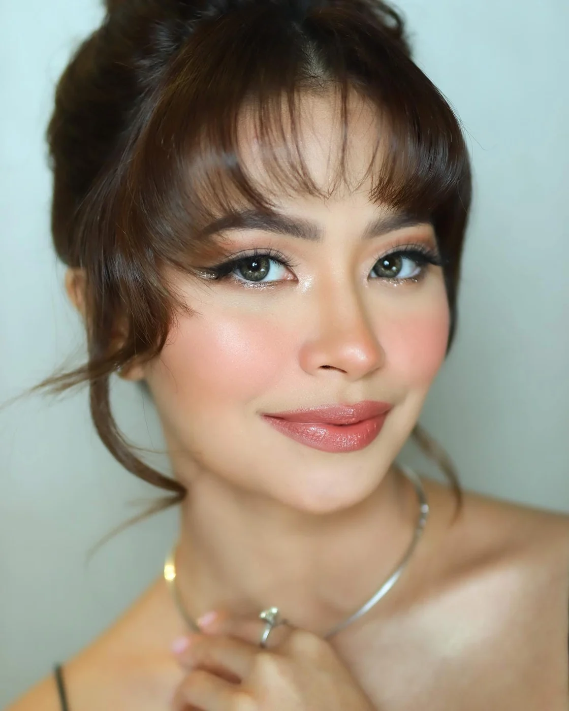 Close-up portrait with a wispy fringe, shimmering eye makeup and a glossy peach lip